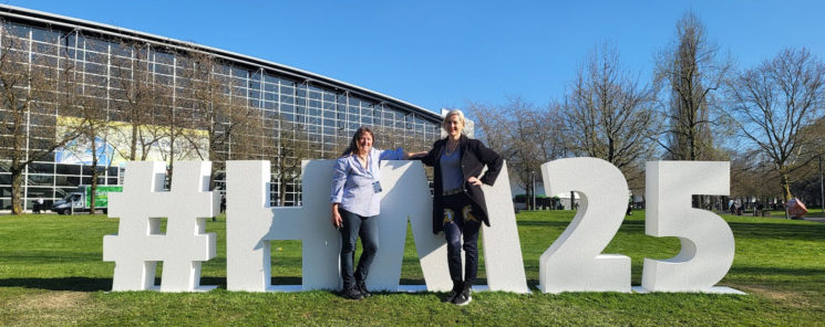 Hannover Messe 2025 Gil Leichtle vom FrauenBranchenBuch und Linkaufbau Expertin Anna Pianka von ABAKUS Internet Marketing mit dem Hannover Messe 2025 Buchstaben-Aufsteller auf der Wiese auf dem Messegelände